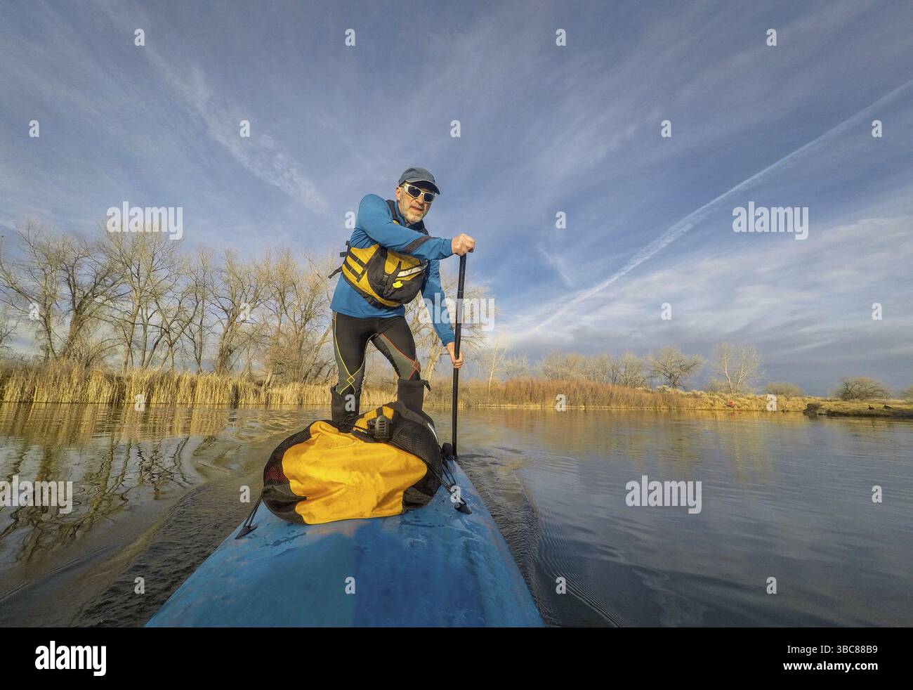 Senior paddler maschio su stand up paddleboard su di un lago calmo in Colorado, paesaggio invernale senza neve Foto Stock