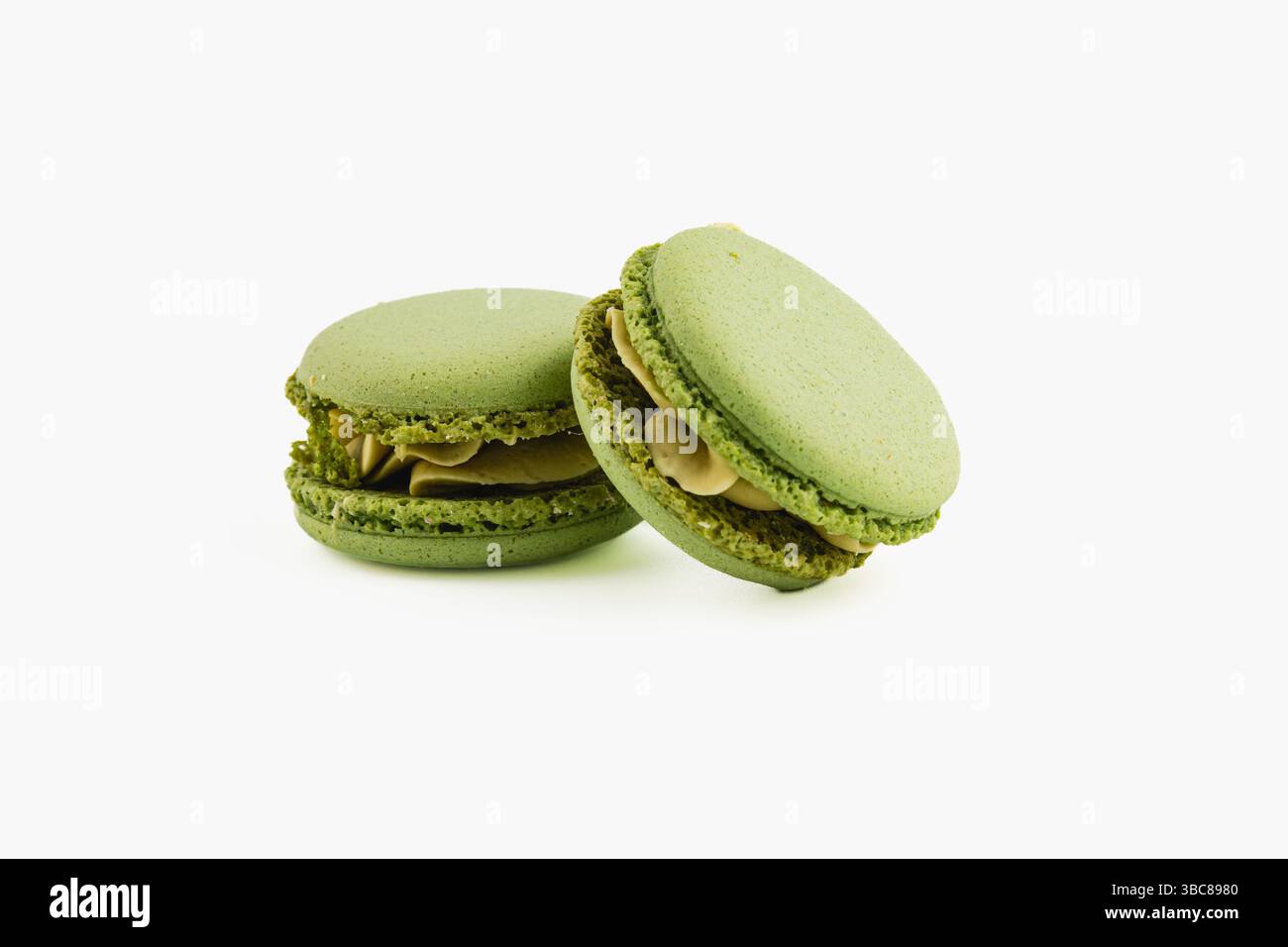 Due macaron verdi si trovano fianco a fianco, con un ripieno cremoso di noci. Il colore brillante e la consistenza liscia mettono in risalto il delicato lavoro di pasticceria che si cela dietro di loro Foto Stock