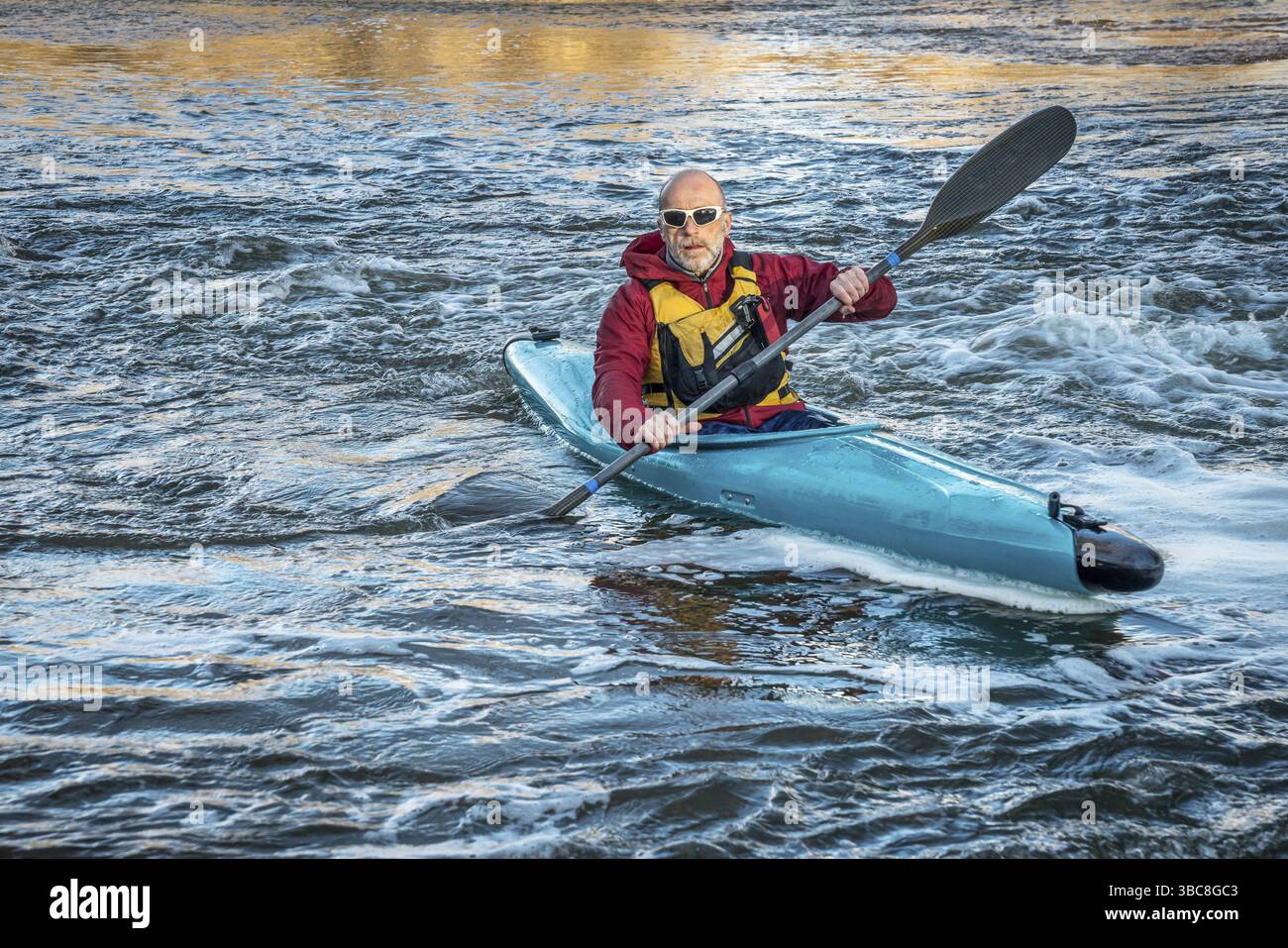 Uomo anziano che pagaia su un fiume turbolento in kayak Foto Stock