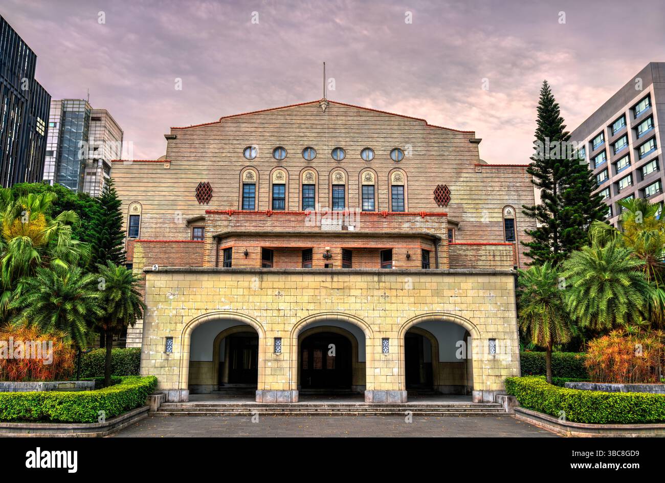 Vista del tramonto della Zhongshan Hall, uno storico auditorium pubblico a Taipei, Taiwan, noto per la sua maestosa facciata in mattoni, ingressi ad arco e una miscela di influenze architettoniche occidentali e orientali. Circondata da un paesaggio lussureggiante e da edifici moderni, la sala si erge come punto di riferimento culturale e civico nel cuore della città Foto Stock