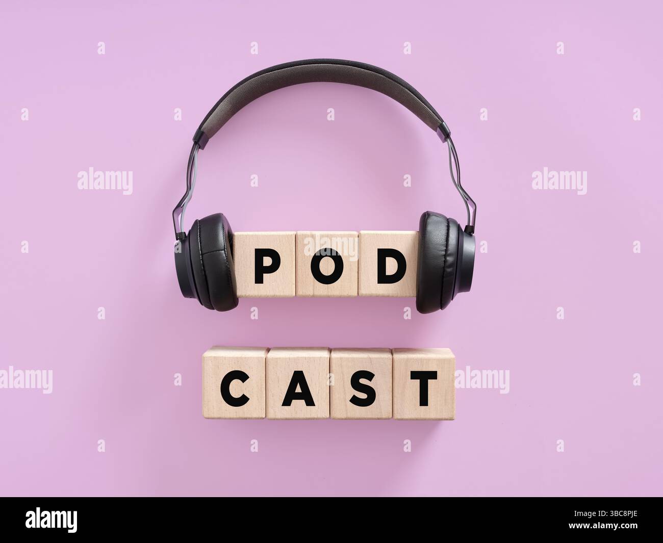 Le cuffie sono appese su cubi di legno che formano la parola podcast, su uno sfondo viola, che rappresenta il concetto di creazione di contenuti audio Foto Stock