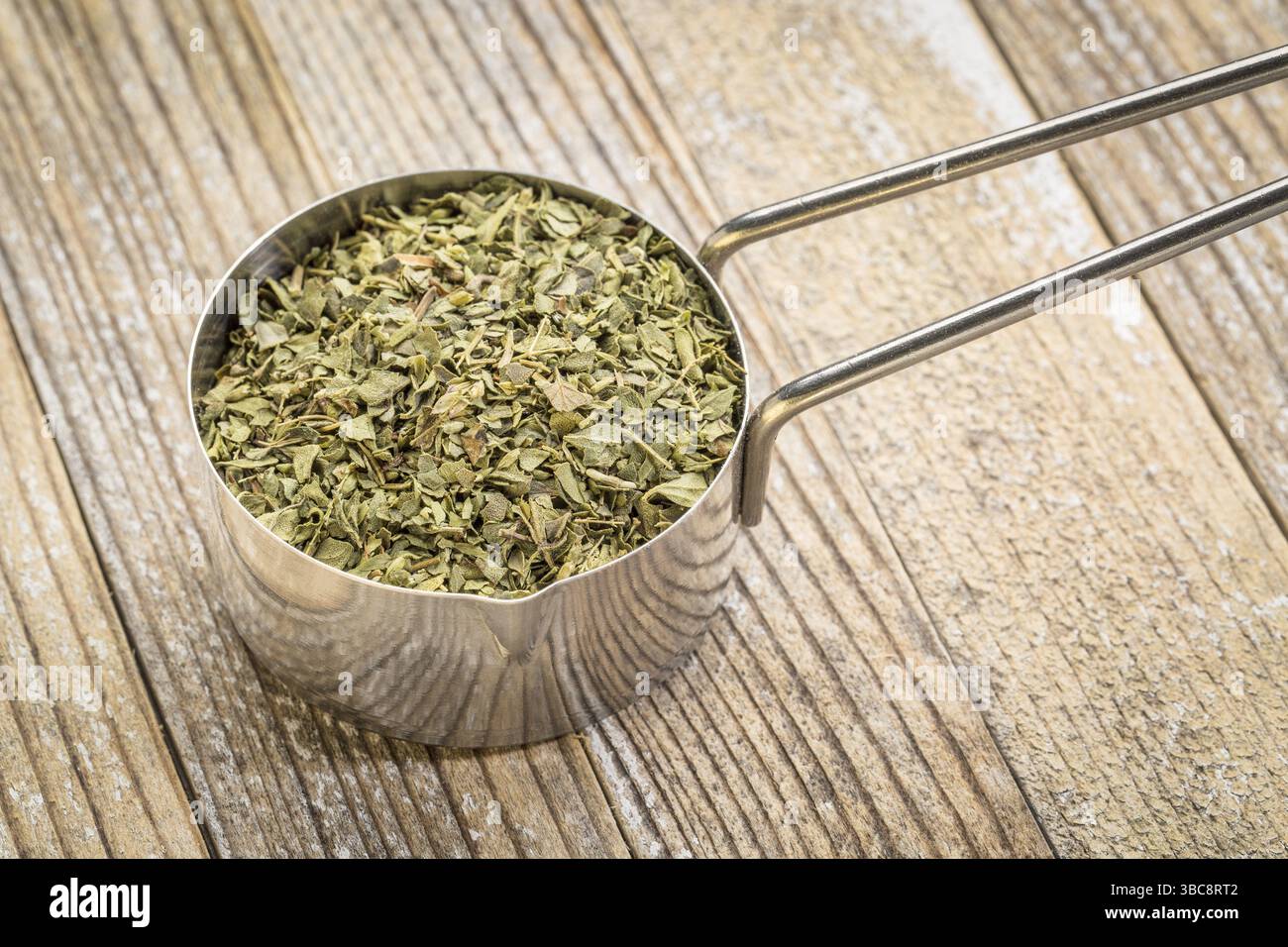 Foglia di origano in un misurino metallico su fondo in legno grunge Foto Stock