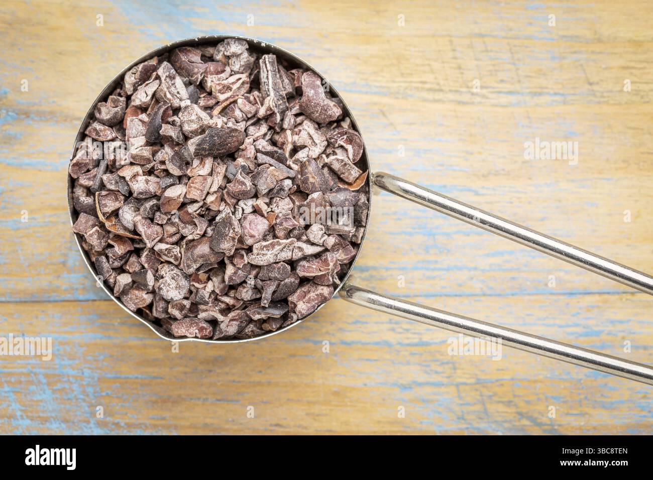 Raw pennini di cacao in un metallo misurino contro dipinta sullo sfondo di legno Foto Stock