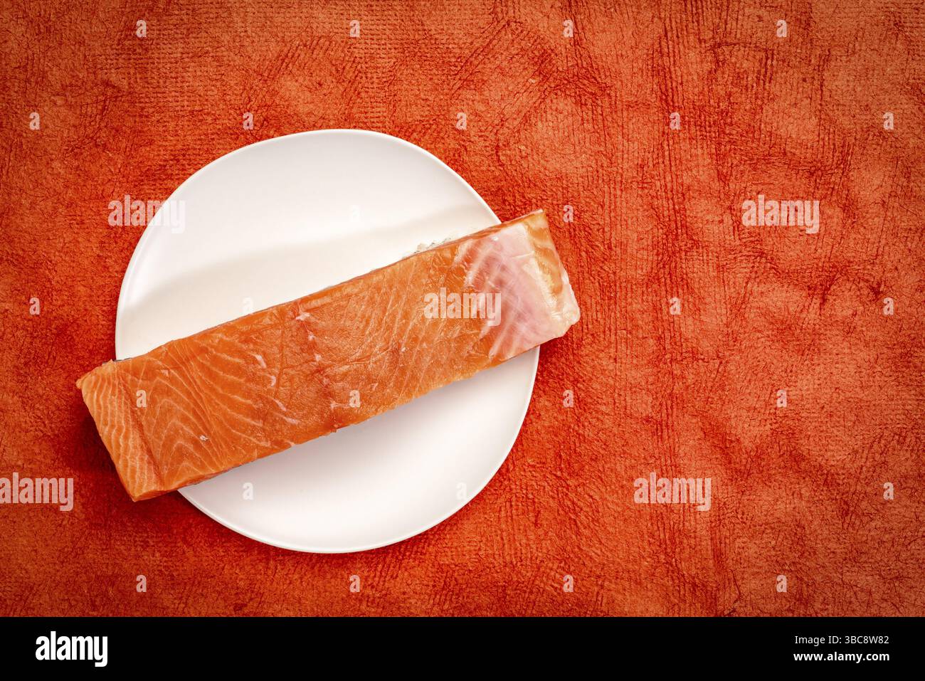 Filetto di salmone greggio selvatico su un piatto bianco su sfondo rosso Foto Stock Filetto di salmone greggio selvatico su un piatto bianco su sfondo rosso Foto Stock