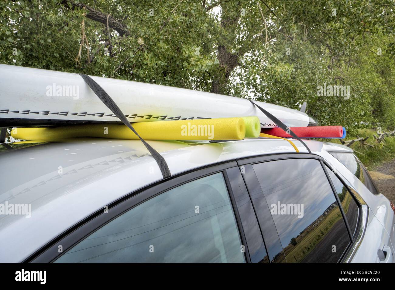 Stand up paddleboard sul tetto di un'auto a noleggio, montaggio improvvisato con cinghie e spaghetti in schiuma per piscina Foto Stock