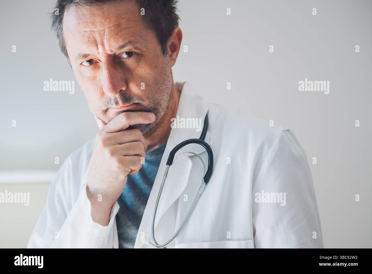 Ritratto di medico maschio serio professionista in cappotto bianco che indossa stetoscopio intorno al collo in ospedale ufficio, messa a fuoco selettiva Foto Stock