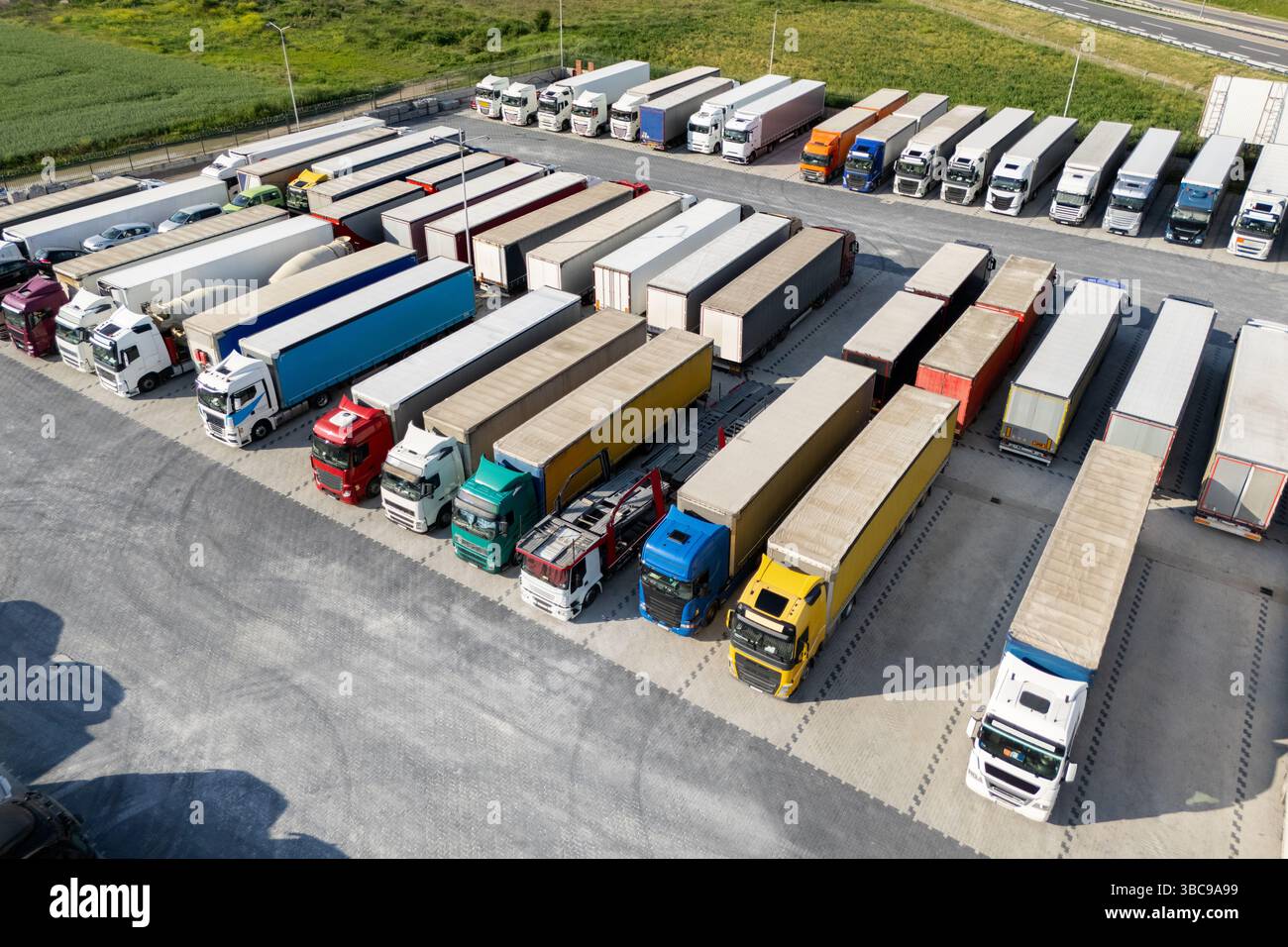 Vista aerea di un ampio parcheggio per camion in un hub logistico, con più semi-camion commerciali parcheggiati in file organizzate. Foto Stock