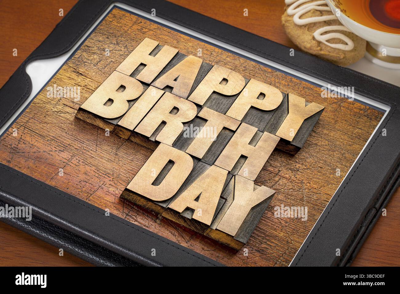 Happy birthday greeting card - word abstract in rilievografia tipo di legno sulla tavoletta digitale con una tazza di tè e cookie Foto Stock