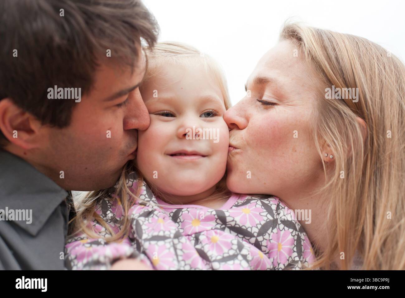 Mamma e papà danno baci alla loro bambina in rosa. Foto Stock