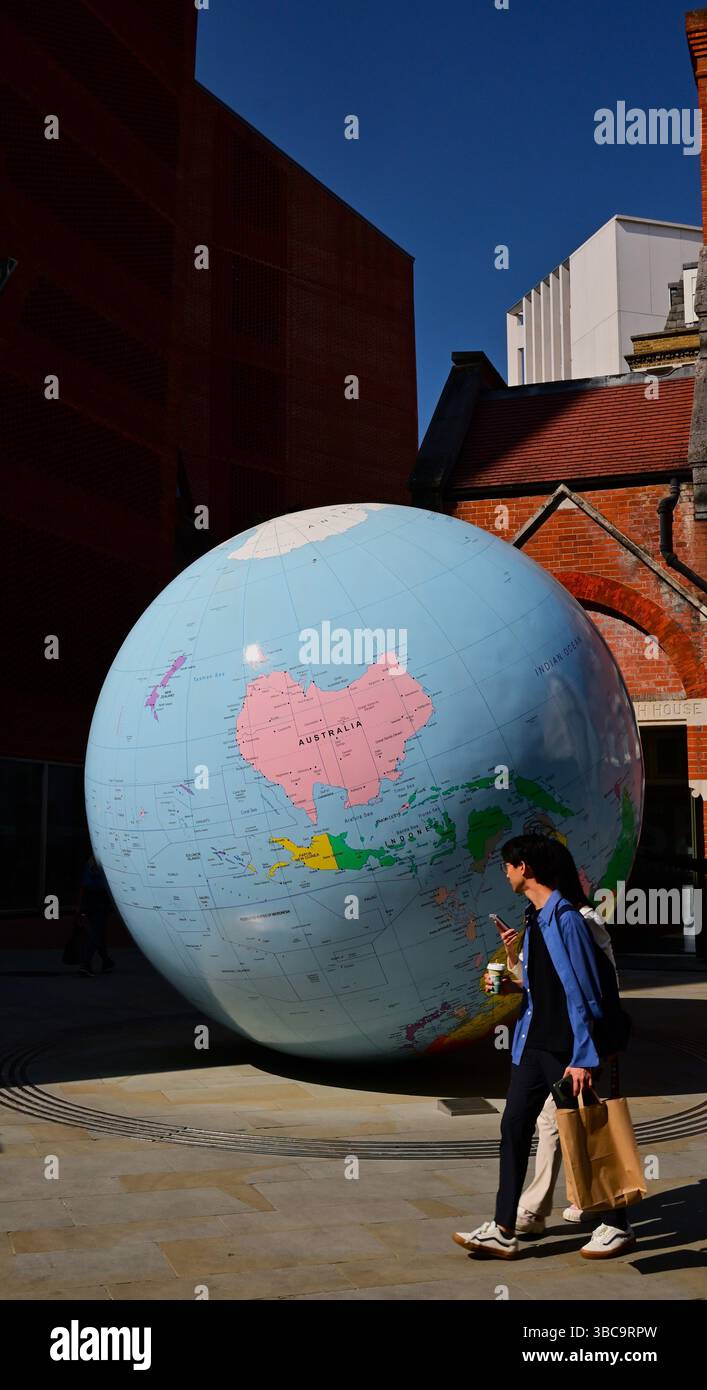 Un Hugh Globe del pianeta Terra in una strada stretta con giovani che camminano nella City di Londra, in Inghilterra Foto Stock