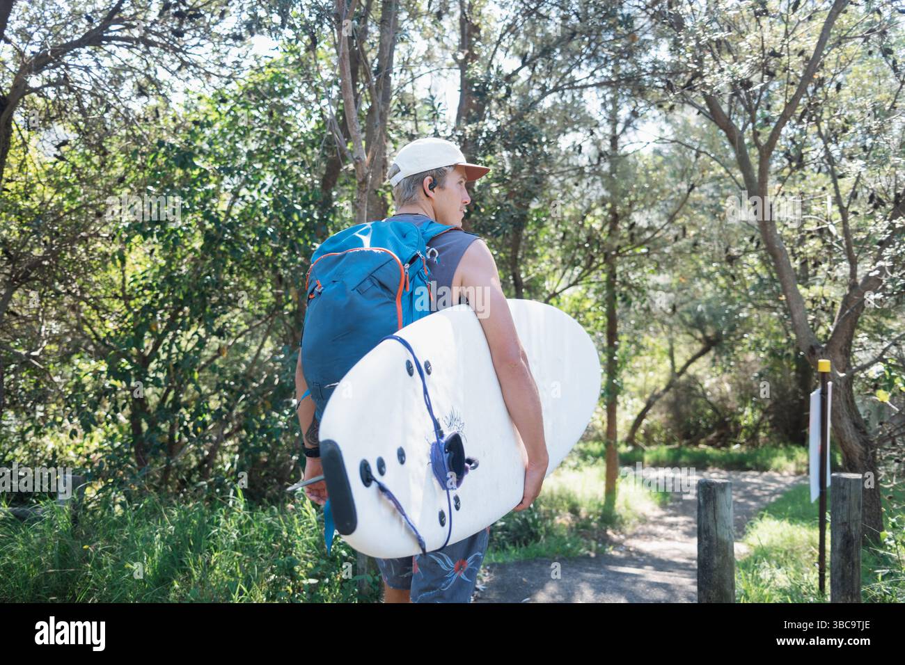 Il surfista cammina lungo il sentiero della foresta con tavola da surf e zaino Foto Stock