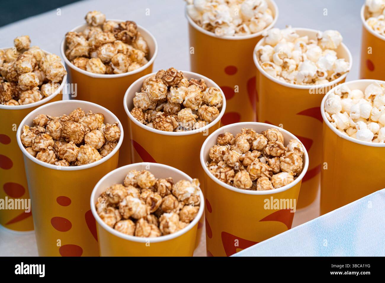 Tazza di carta con snack di popcorn sul tavolo. deliziosi popcorn bruno al caramello. in un primo piano di vetro giallo arancione. scatole di popcorn in vendita sul c Foto Stock