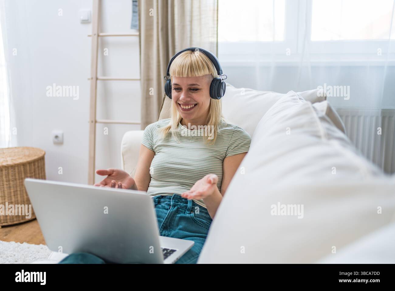 Una giovane donna scambia lo studente seduto sul divano di casa utilizzando un computer portatile con cuffie wireless per lavorare in remoto partecipando a lezioni virtuali e riunioni video Foto Stock