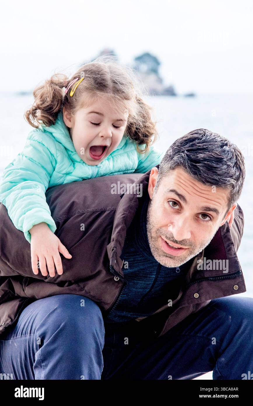 Padre e figlia di famiglia che camminano fuori in autunno, uomo e ragazza in giacca che ingannano e giocano Foto Stock