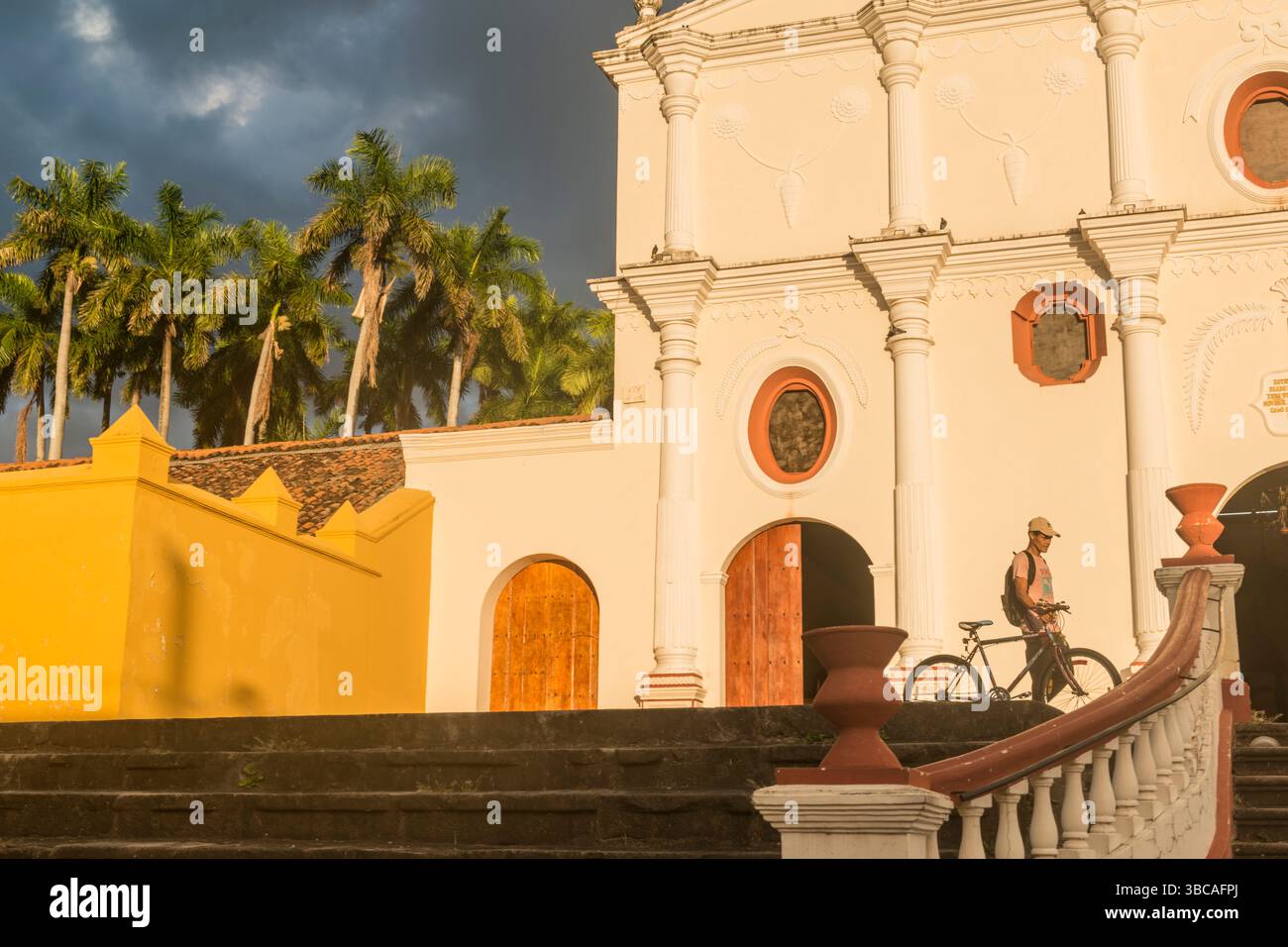 Uomo che spinge la bicicletta di fronte alla parete color ocra della Cattedrale di San Francisco e del suo museo al crepuscolo. Granada, Nicaragua. Foto Stock