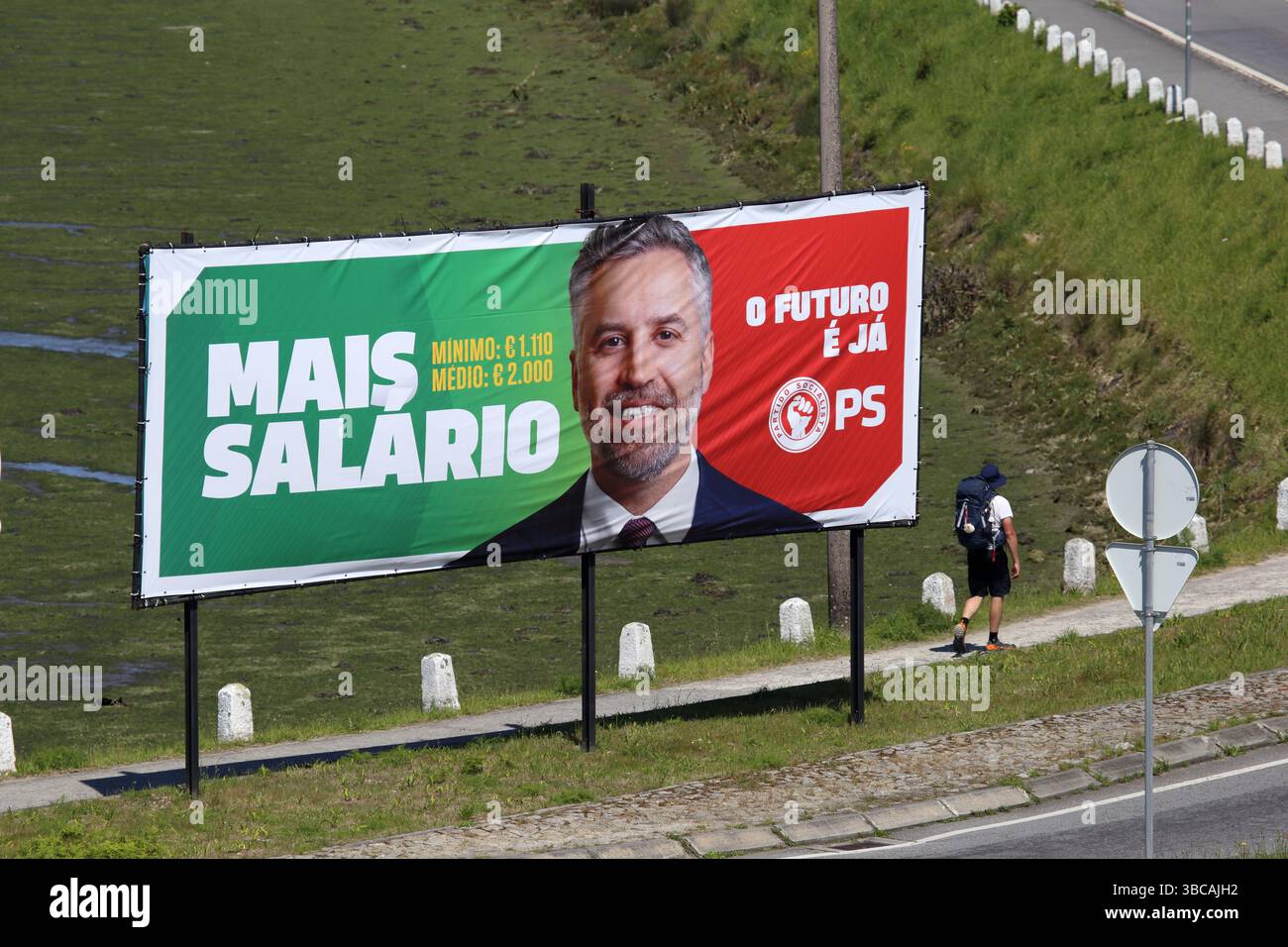 Viana do Castelo, Portogallo - 15 maggio 2025: Un pellegrino passa davanti a un cartellone della campagna del Partito Socialista che promuove aumenti salariali prima delle elezioni Foto Stock