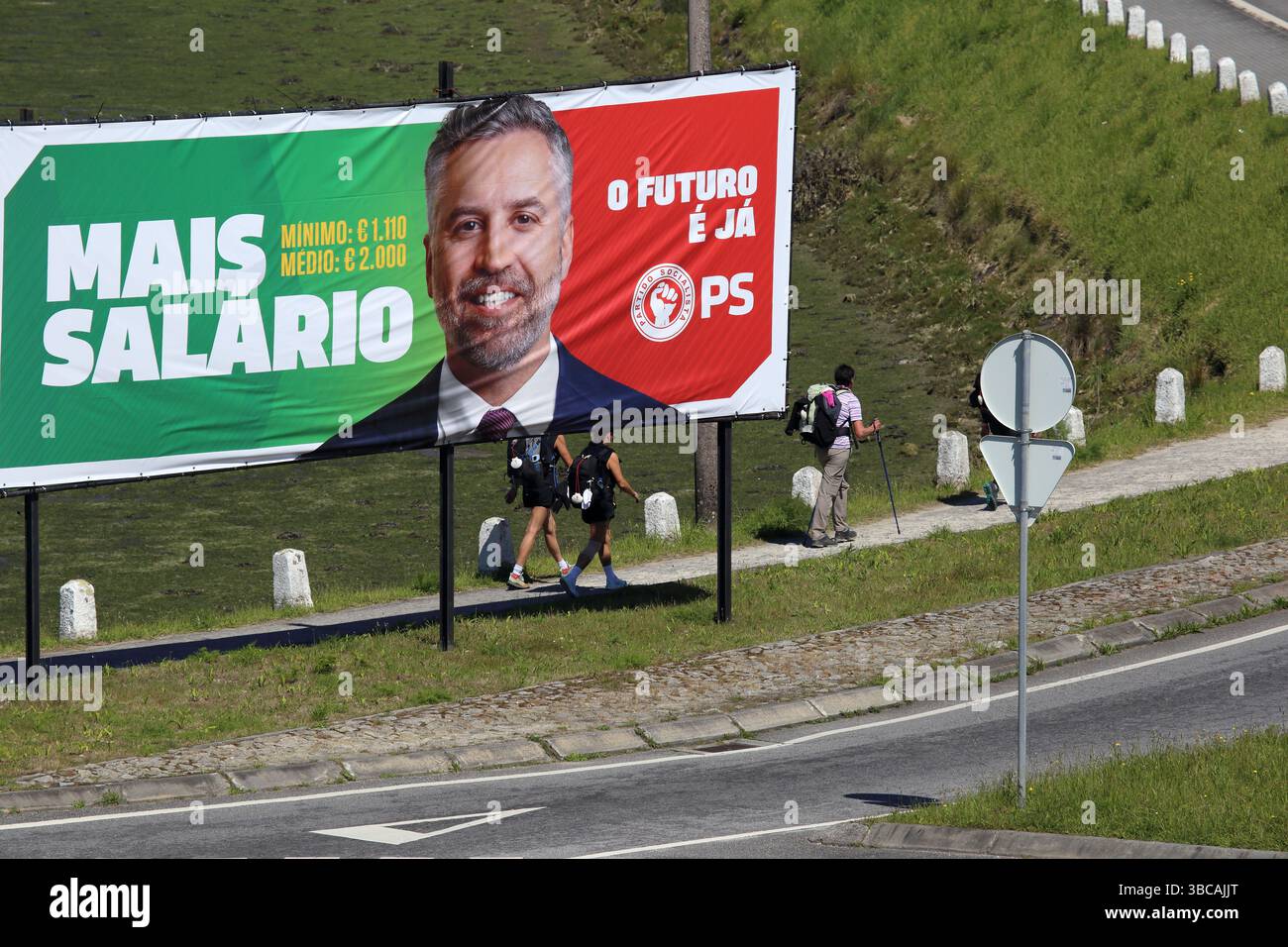 Viana do Castelo, Portogallo - 15 maggio 2025: I pellegrini passano davanti a un cartellone della campagna del Partito Socialista che promuove l'aumento dei salari prima del giorno delle elezioni Foto Stock