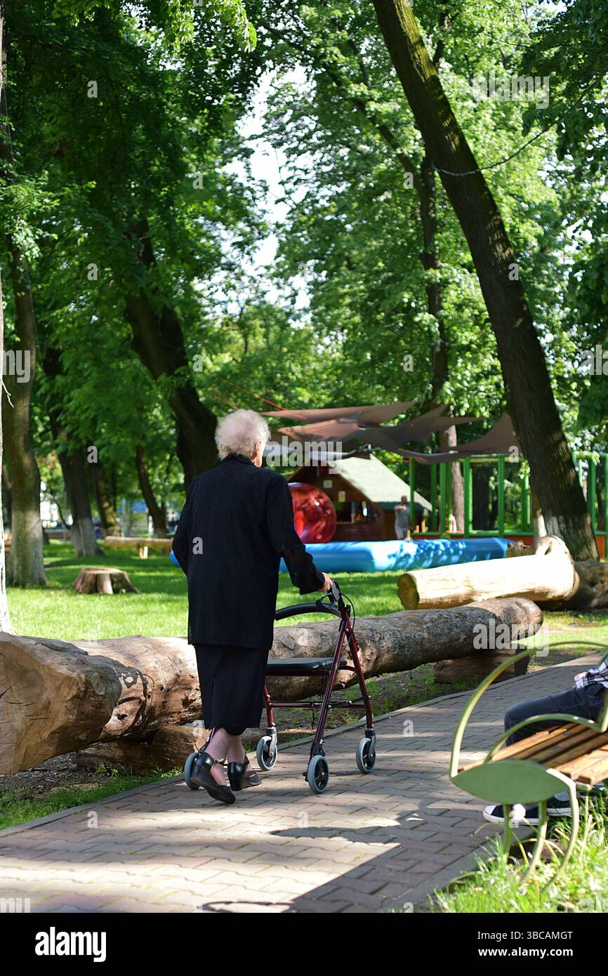 Una vecchia signora che fa una passeggiata nel parco con un camminatore Foto Stock