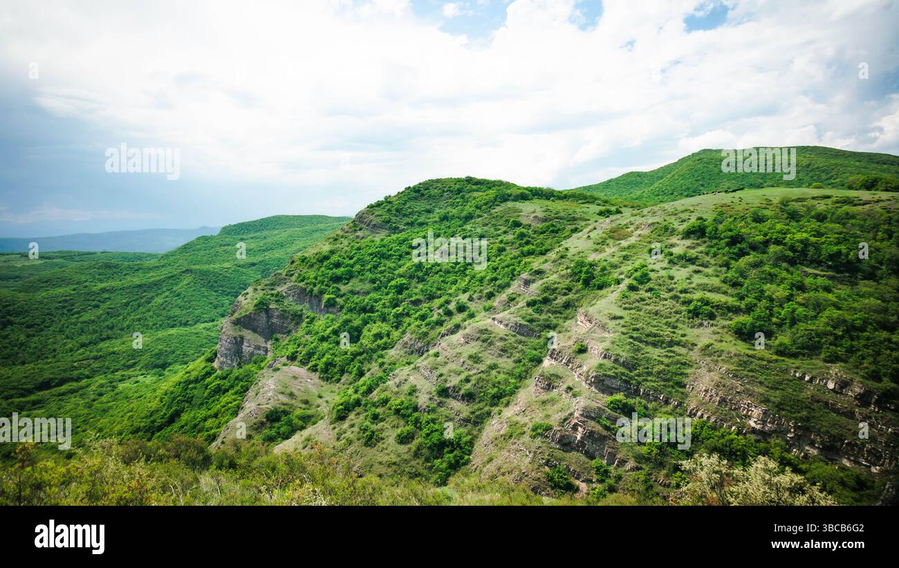 Pendii verdi e luminosi con strati rocciosi stratificati sotto un cielo parzialmente nuvoloso. Vivaci texture naturali nella natura selvaggia georgiana Foto Stock