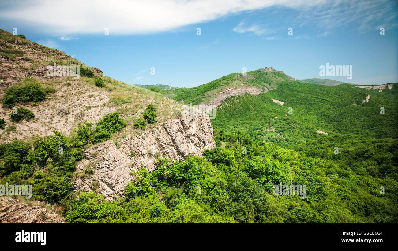 Pendii verdi e luminosi con strati rocciosi stratificati sotto un cielo parzialmente nuvoloso. Vivaci texture naturali nella natura selvaggia georgiana Foto Stock
