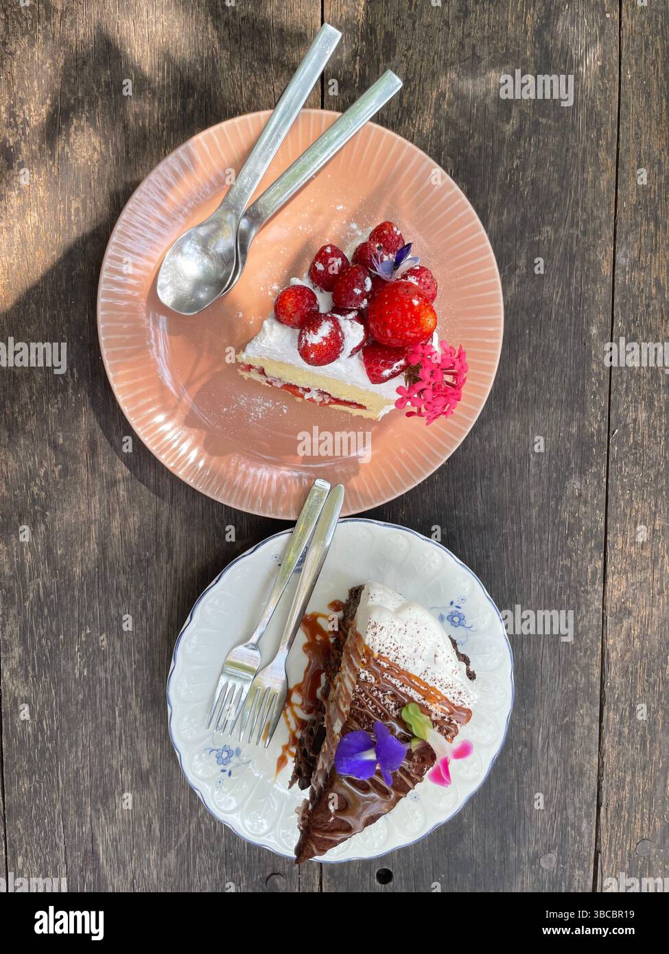 Due fette di torta sui piatti: Shortcake alle fragole e torta al caramello al cioccolato con panna montata, servita su un rustico tavolo di legno. - Immagine stock catturata con smartphone