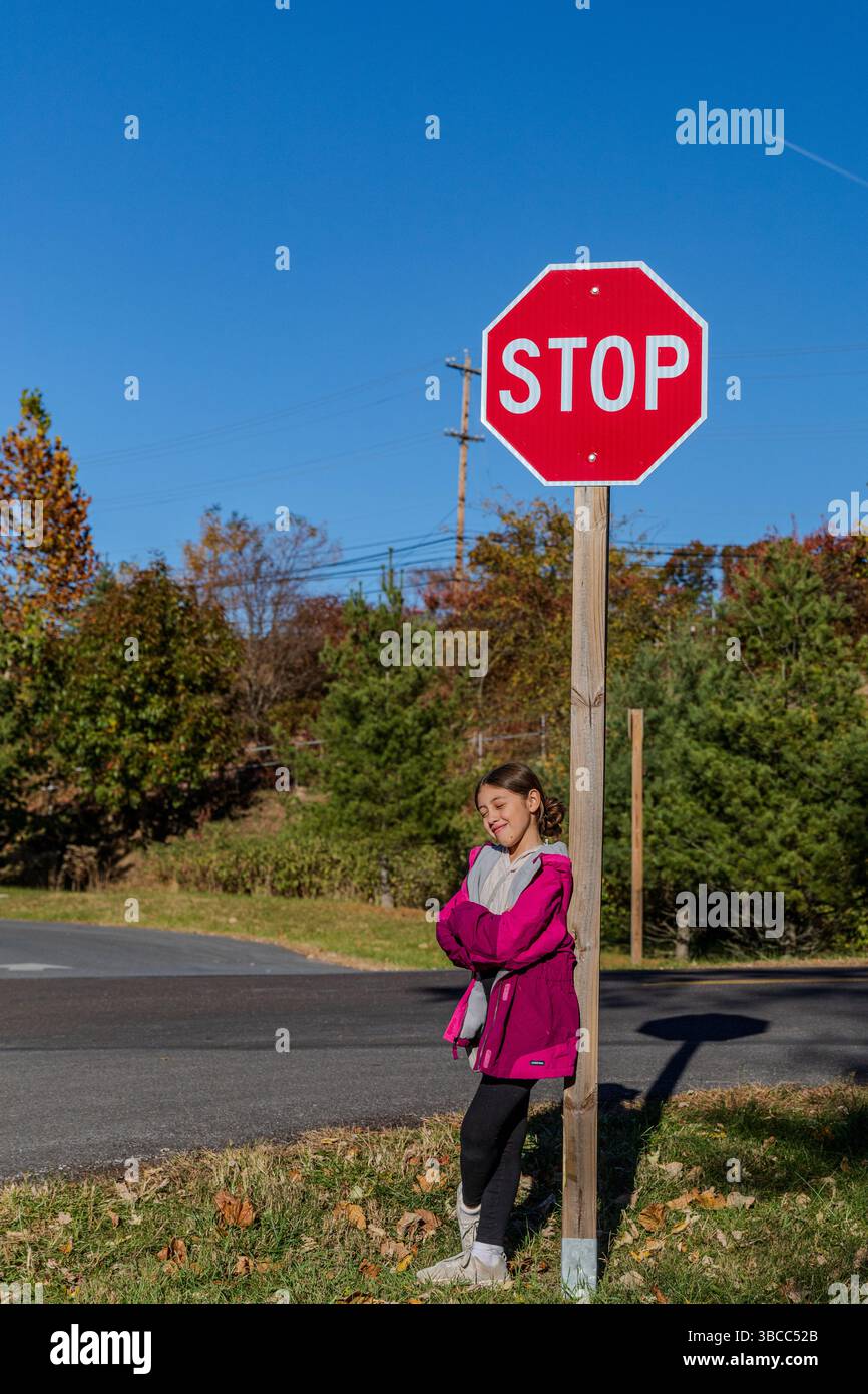 Una ragazza sta di fronte a un segnale di stop. Indossa una giacca rosa e sorride Foto Stock Una ragazza sta di fronte a un segnale di stop. Indossa una giacca rosa e sorride Foto Stock