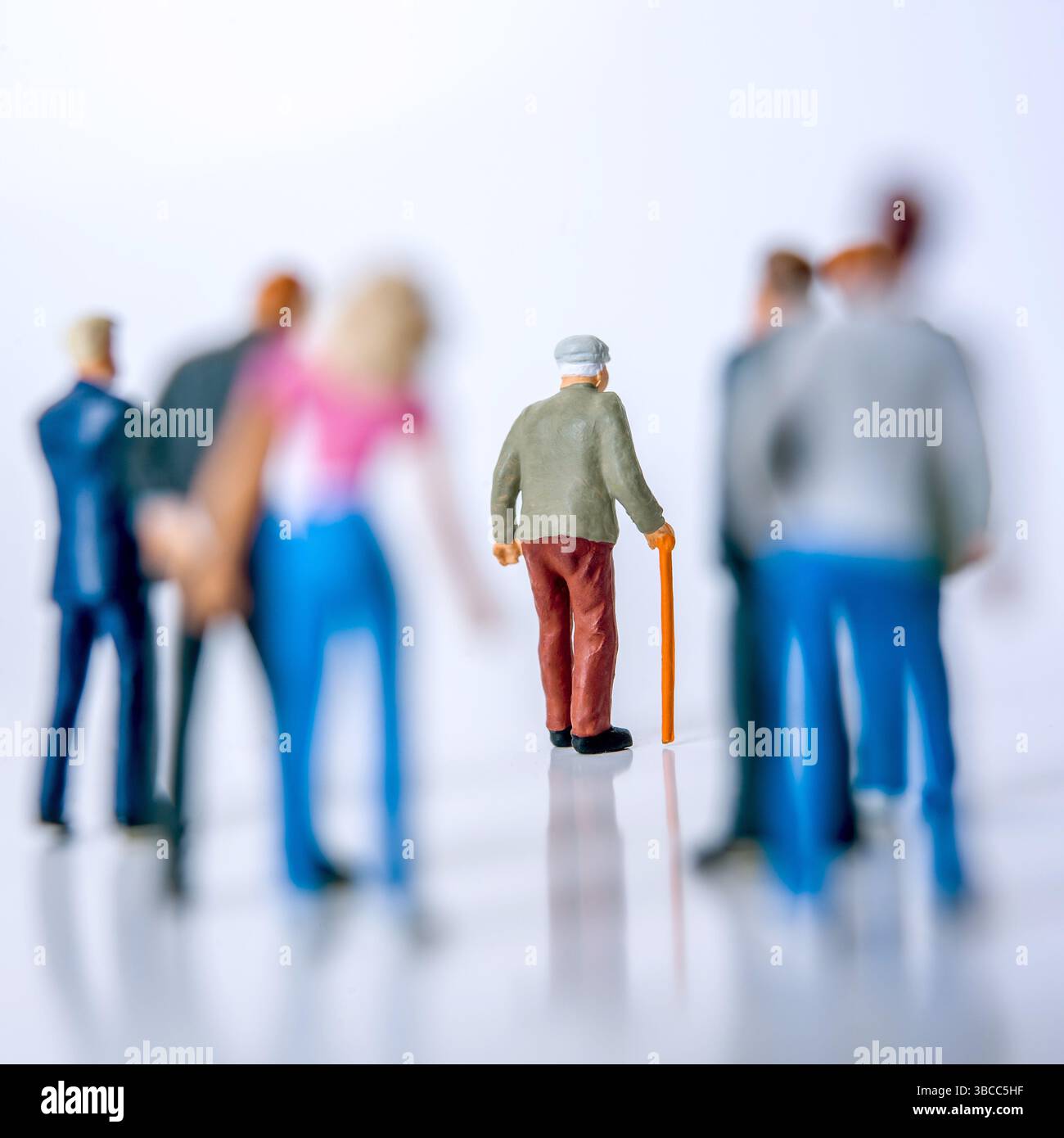 Un gruppo di statuine si trova dietro un uomo anziano con un bastone, che sta camminando in avanti Foto Stock