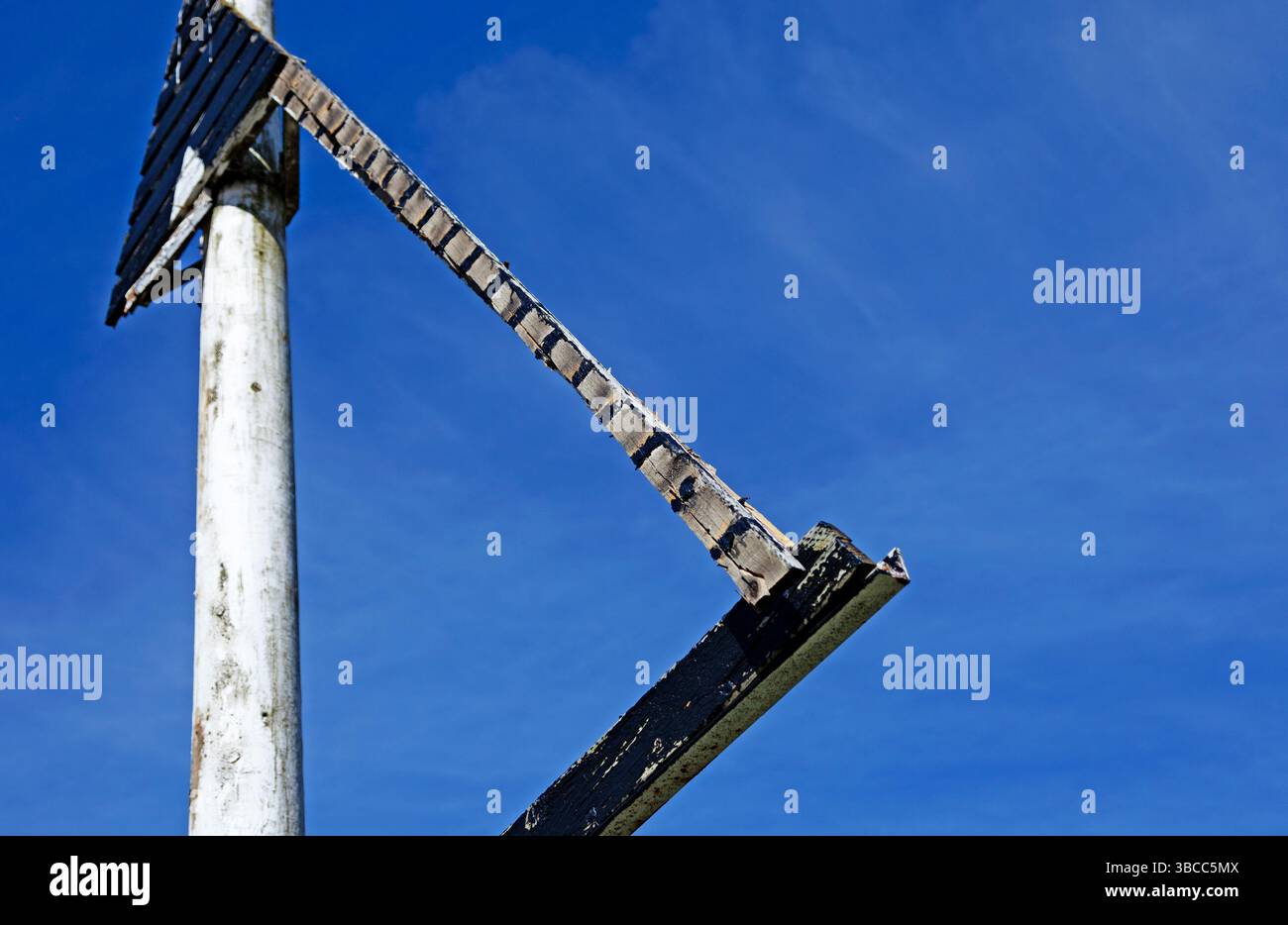 Una struttura in metallo triangolare resistente agli agenti atmosferici, montata su un palo bianco, si staglia fortemente contro un cielo blu vibrante, creando una silhouette geometrica forte Foto Stock