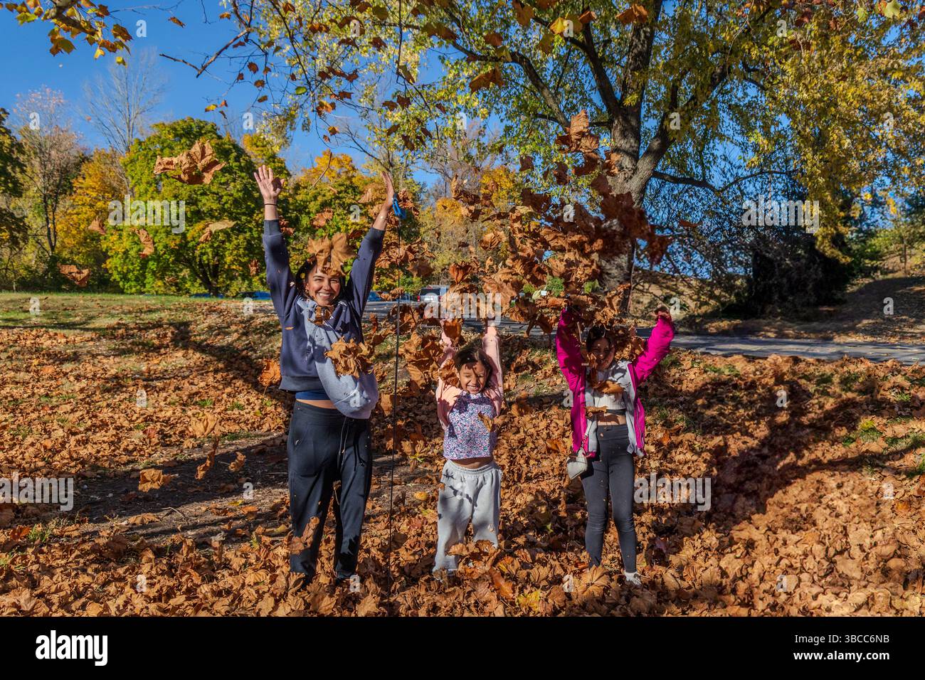 Una famiglia di tre persone sta giocando nelle foglie, con il padre che tiene un bambino. La scena è gioiosa e giocosa, in quanto la famiglia si sta divertendo a divertirsi Foto Stock Una famiglia di tre persone sta giocando nelle foglie, con il padre che tiene un bambino. La scena è gioiosa e giocosa, in quanto la famiglia si sta divertendo a divertirsi Foto Stock