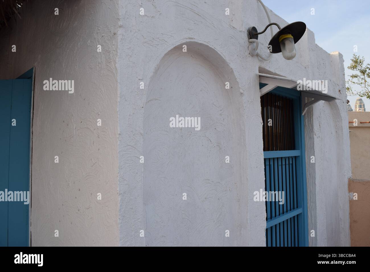 Fascino minimalista della tradizionale architettura del Qatar con pareti bianche rustiche e una porta di legno blu cielo Foto Stock