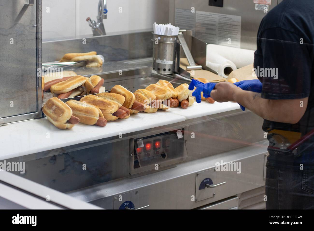 Un dipendente della Costco indossa i guanti prima di inzuppare gli hot dog nella cucina del food Court di un negozio Costco a Wilsonville, Oregon. Foto Stock
