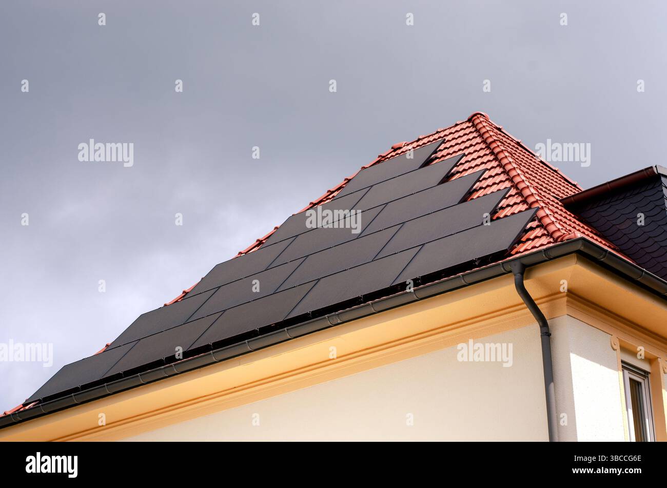 Pannelli solari integrati in un tetto piastrellato rosso di un edificio residenziale sotto un cielo nuvoloso. Foto Stock