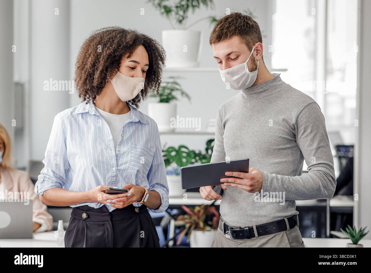 Idee di marketing per il lavoro e la protezione contro le epidemie. Il manager mostra la signora afroamericana in un tablet con maschera protettiva con un compito vicino al posto di lavoro Foto Stock