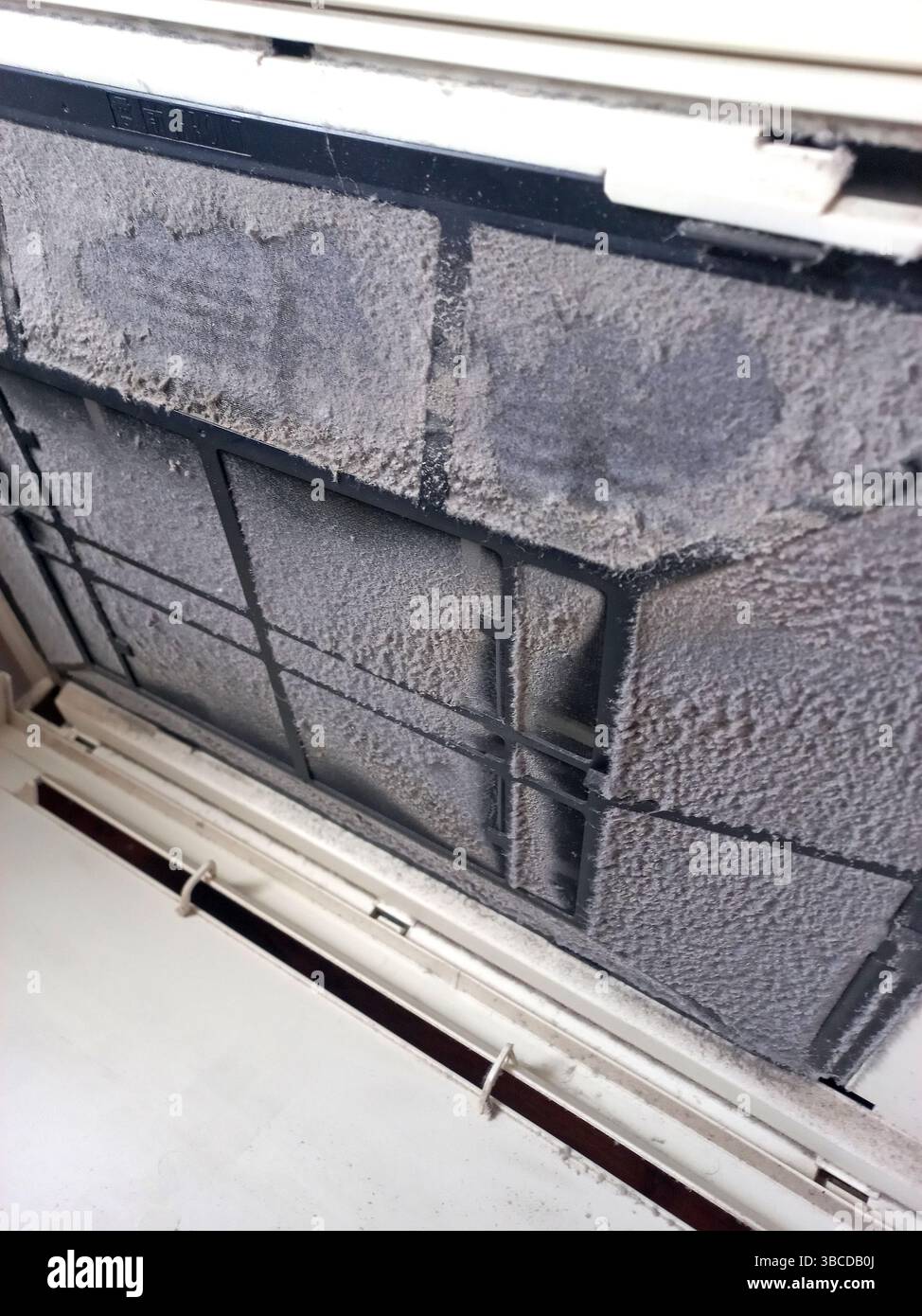 Primo piano di un filtro del condizionatore d'aria domestico fortemente ostruito da polvere e detriti che mostra una manutenzione scadente e potenziali rischi per la salute respiratoria Foto Stock