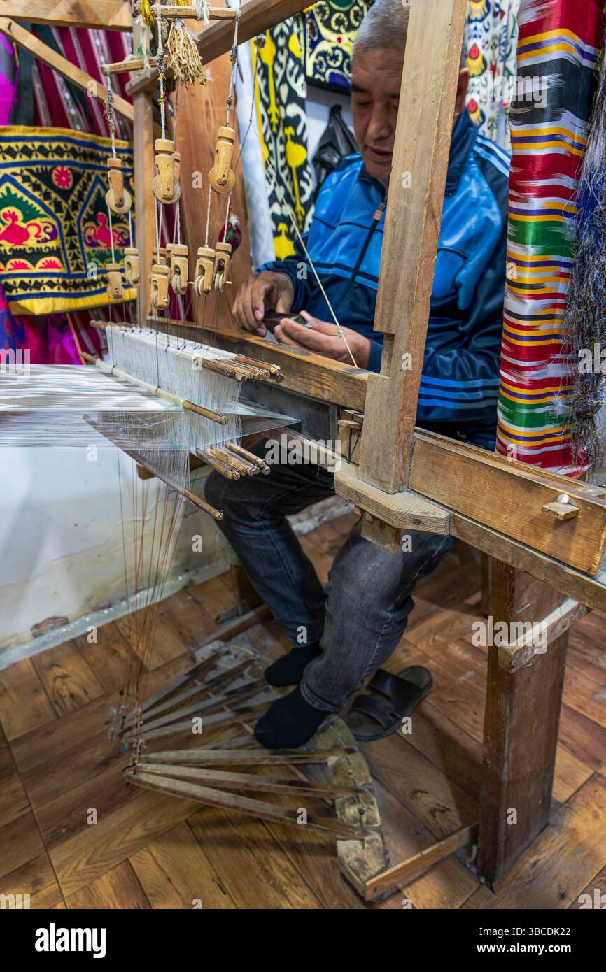 Un artigiano Bukhara in Uzbekistan lavora su un telaio tradizionale, tessendo tessuti colorati che riflettono secoli di patrimonio artigianale locale. Foto Stock