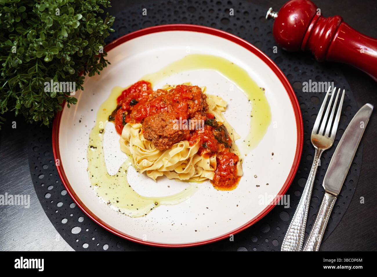 Deliziose tagliatelle condite con polpette succose in una ricca salsa di pomodoro, guarnite con olio d'oliva e pepe nero. Foto Stock