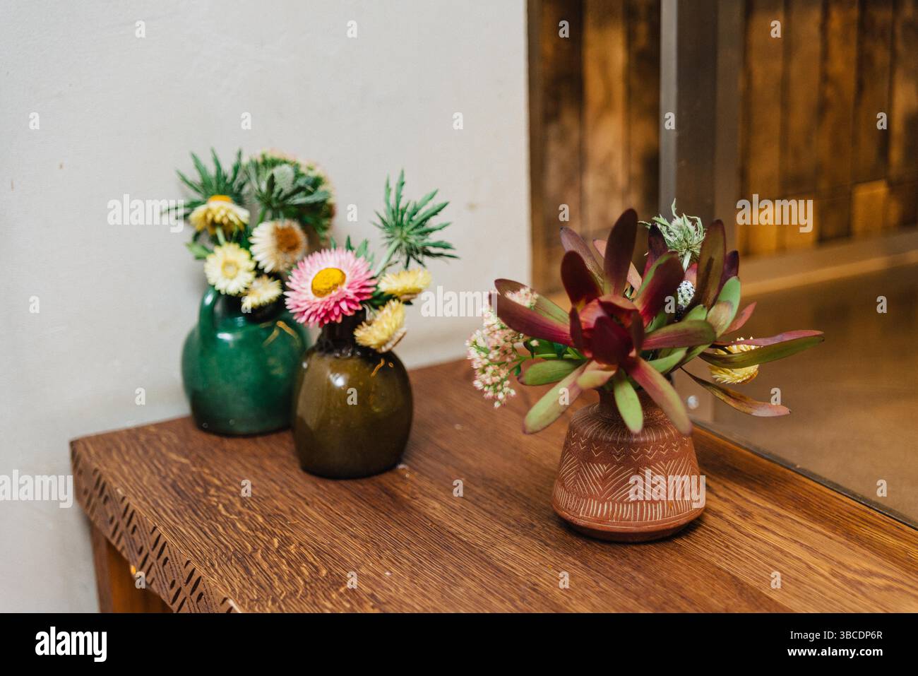 Miniature di fiori secchi e freschi in vasi in ceramica e vetro, disegnati su un tavolo in legno per un arredamento intimo e rustico. Foto Stock