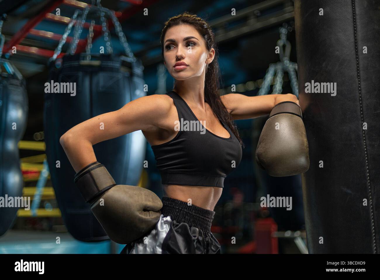 un'abile pugile femminile mostra la sua forza e determinazione in una palestra di allenamento. Indossa guanti e un abbigliamento sportivo che si adatta perfettamente a una pesante borsa da pugni. Foto Stock un'abile pugile femminile mostra la sua forza e determinazione in una palestra di allenamento. Indossa guanti e un abbigliamento sportivo che si adatta perfettamente a una pesante borsa da pugni. Foto Stock