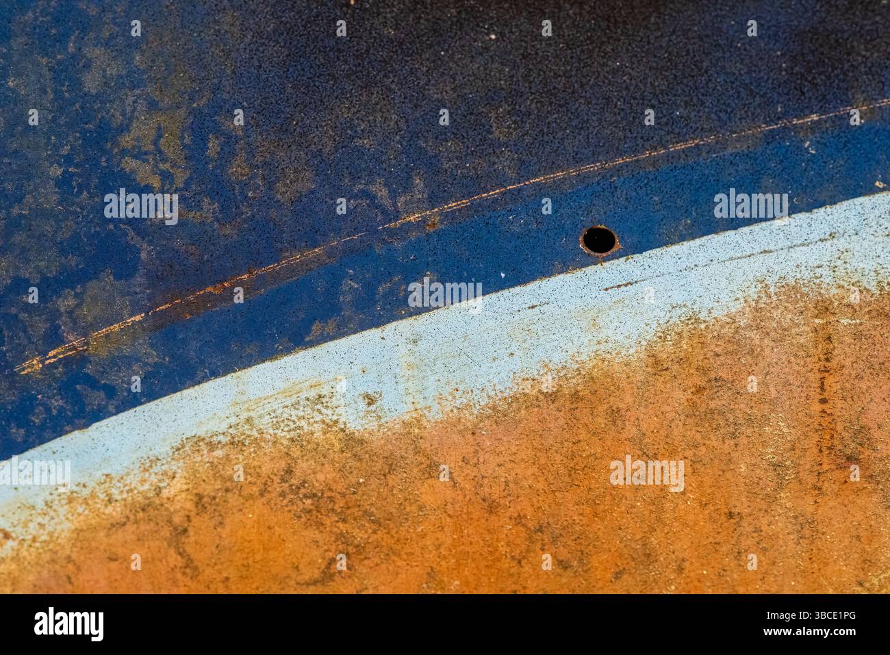 Primo piano di un pannello di un'auto arrugginito con strati di vernice blu, arancione e bianco, che formano una struttura astratta di età, colore e corrosione. Foto Stock