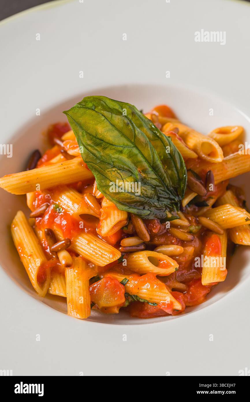 Penne alla arrabiata classica italiana con basilico e salsa su tavolo grigio scuro. Penne arrabbiata con salsa piccante Foto Stock