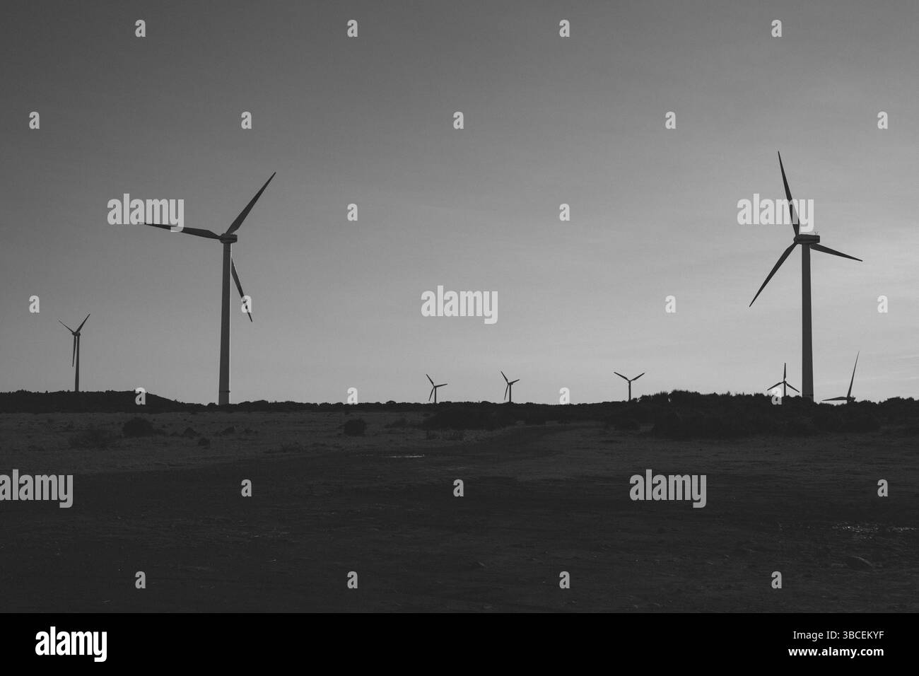 Le turbine eoliche sagomate si stagliano contro un vasto cielo limpido su un paesaggio ondulato Foto Stock