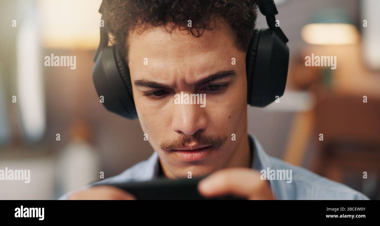 Online, videogiochi e uomo con cuffie, smartphone e serio per lo sport virtuale in appartamento. Streaming, videogamer e persona con app mobile per Foto Stock