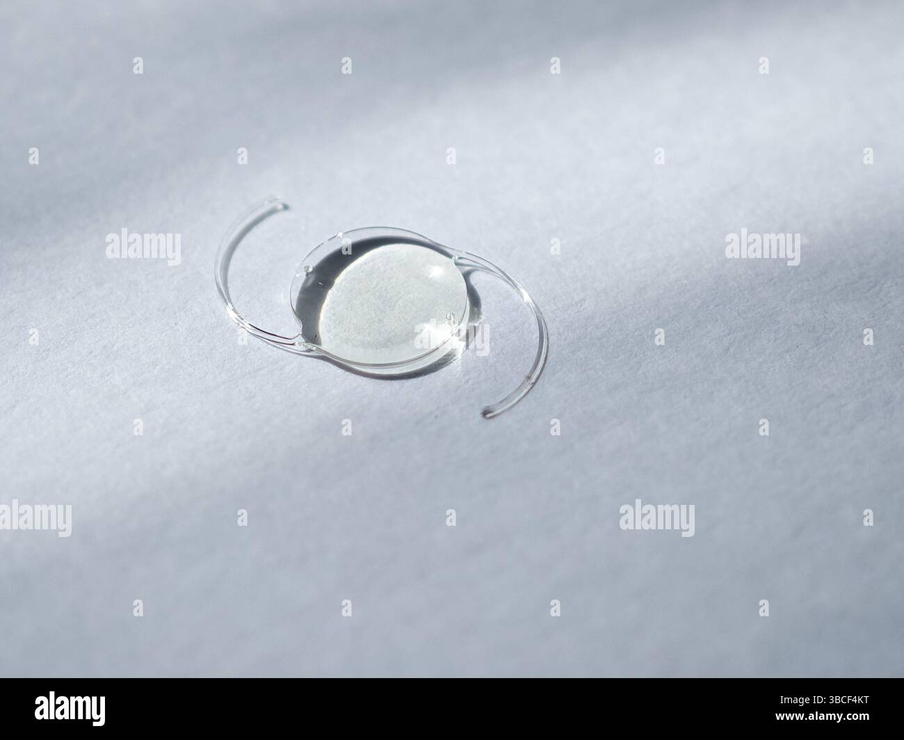 Vista ravvicinata di una lente intraoculare posizionata su una superficie morbida, che mostra la sua struttura trasparente e il design curvo, con un'illuminazione soffusa che crea g Foto Stock