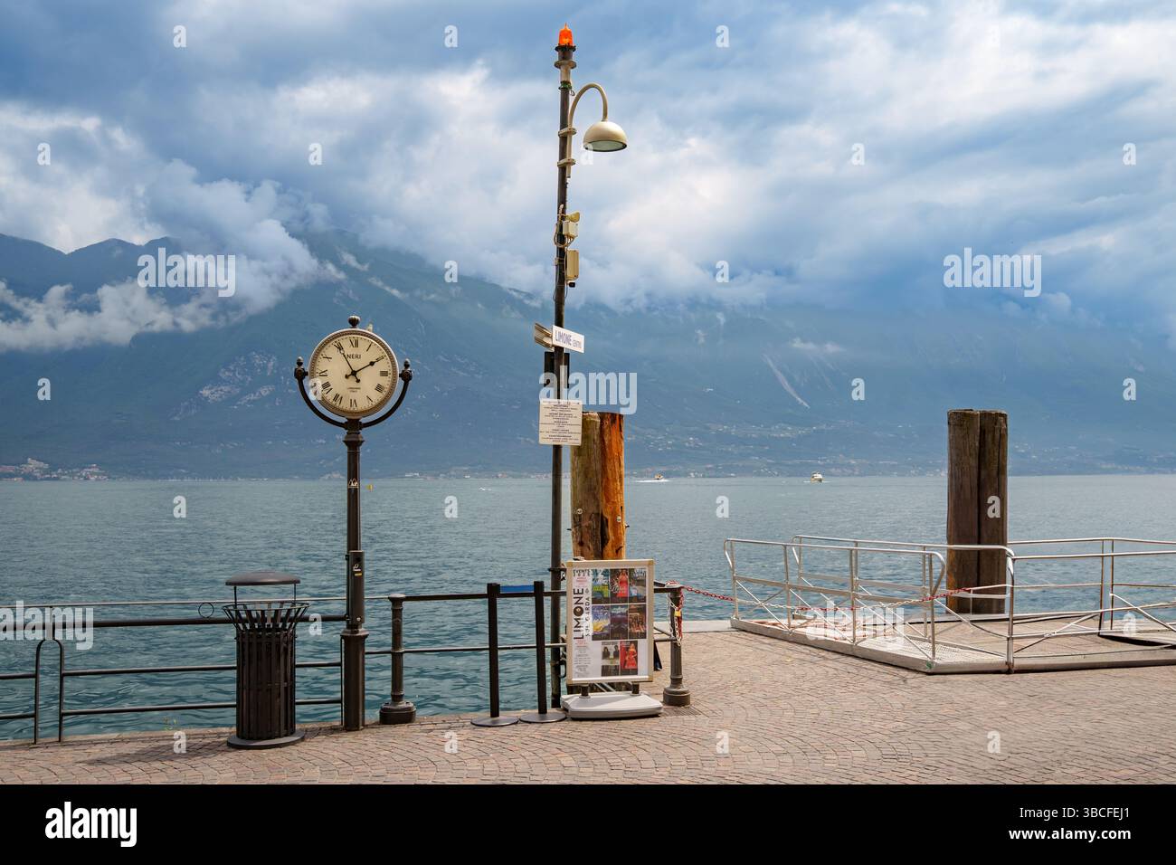 Attracco barche a Limone sul Garda, Lago di Garda, Italia, con grande orologio classico. Monte Baldo sullo sfondo, avvolto nelle nuvole Foto Stock