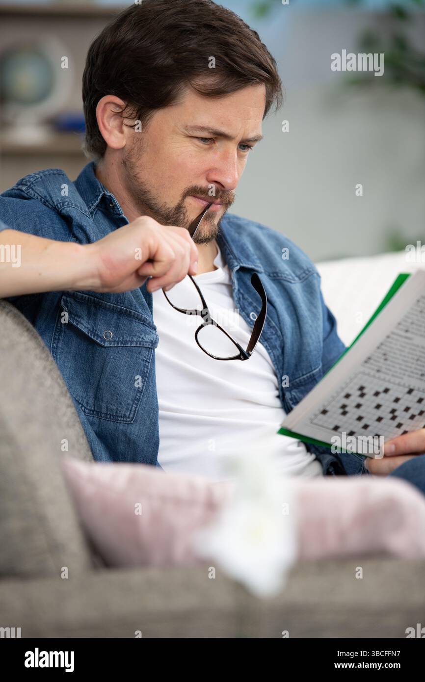 giovane uomo seduto sul divano e facendo cruciverba puzzle Foto Stock
