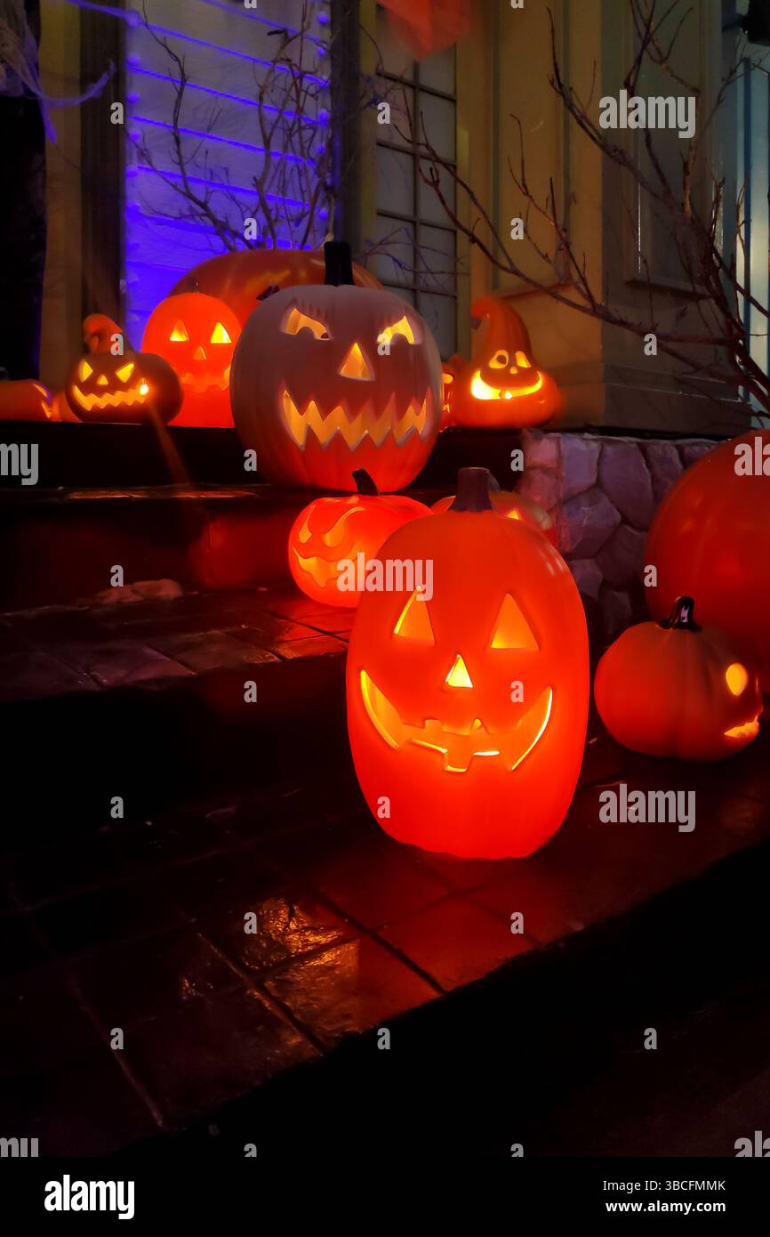 Scena natalizia di Halloween con un gruppo di lanterne di plastica che si illuminano con calore con luci interne. Le zucche sono disposte sui gradini di un Foto Stock