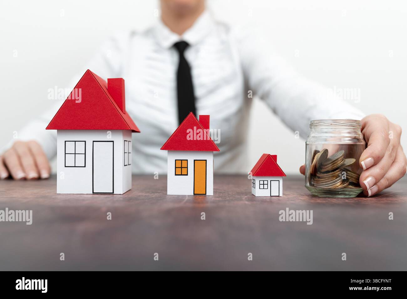 Risparmia per tornare a casa. Risparmio di denaro per la casa e gli immobili. Donna che protegge le mani su monete pila e modello di casa sul tavolo Foto Stock