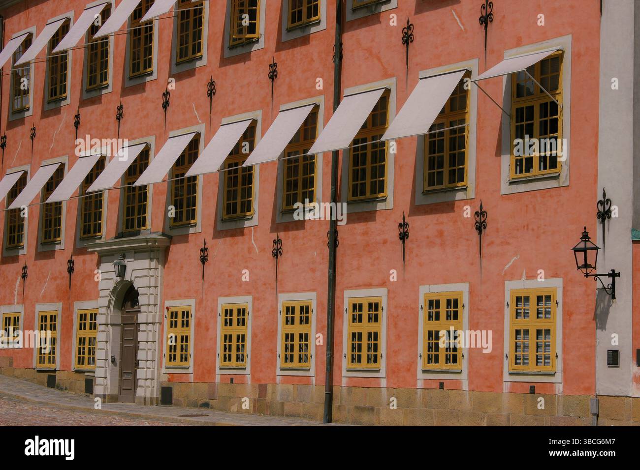 Storico edificio europeo con pareti in stucco color salmone, finestre in legno giallo e tende bianche classiche nella città vecchia di Stoccolma, Svezia. Foto Stock