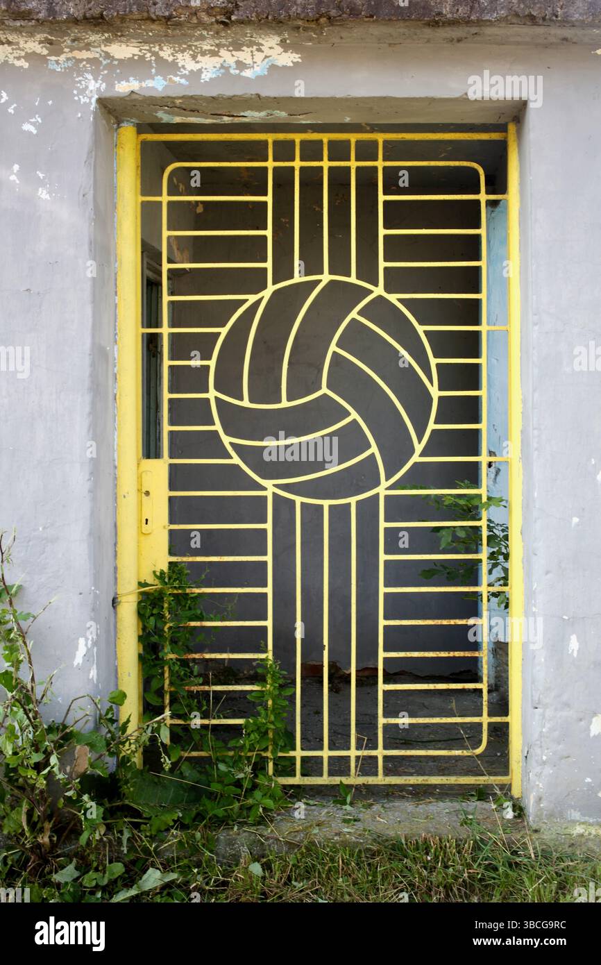 Cancello in metallo giallo con design da calcio davanti al muro di una struttura sportiva. Foto Stock