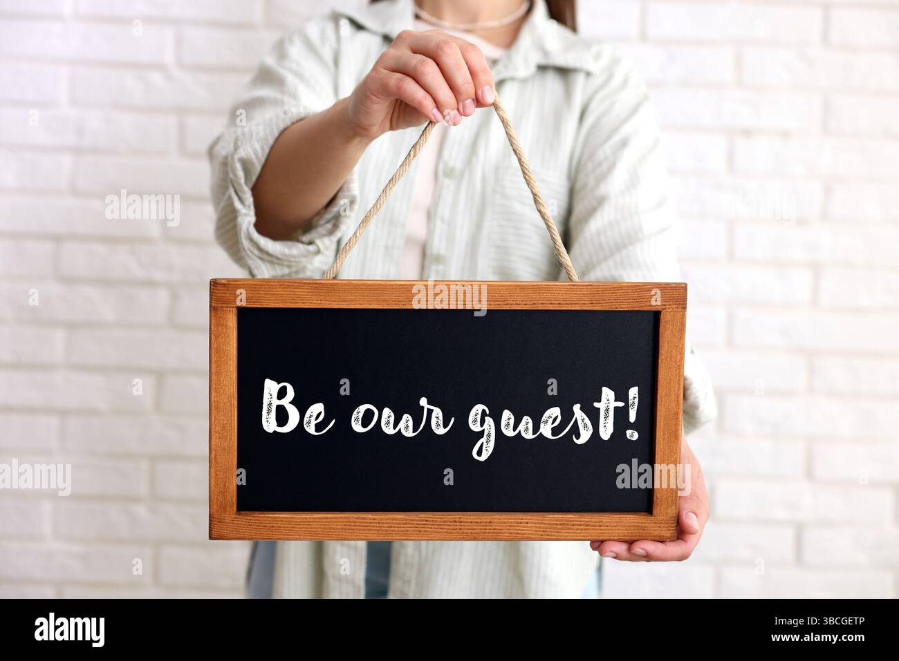 Donna che tiene in mano una piccola lavagna con la frase Be Our Guest indoor, primo piano Foto Stock